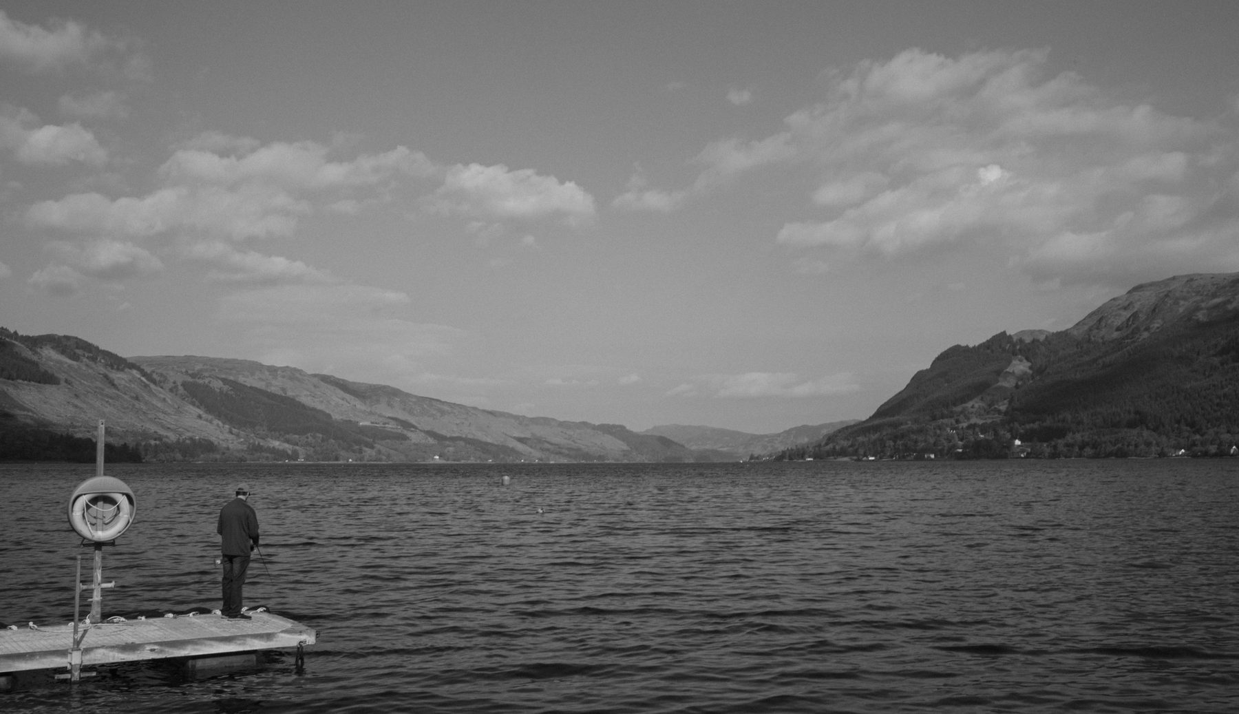 Figure standing on a jetty looking out over Loch Duich, hills receding into the distance
